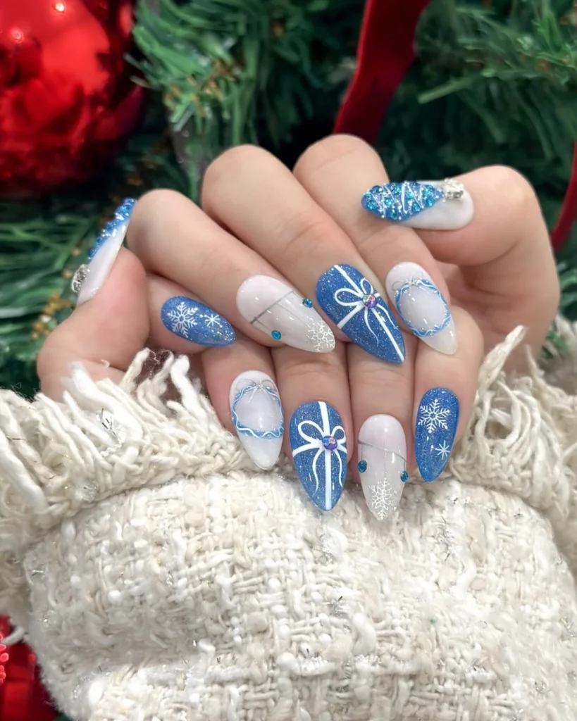 Blue Christmas nail designs with white snowflakes, gift bow nail art, silver glitter, and rhinestone accents.