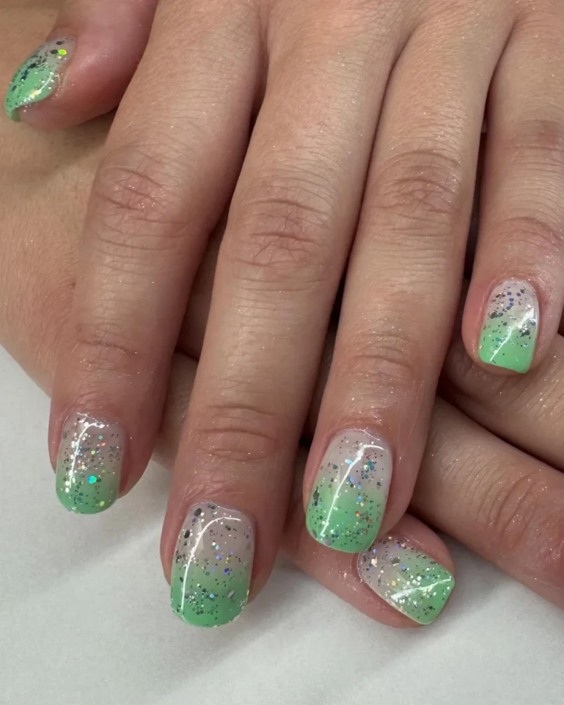 Christmas glitter ombre nail featuring mint green fading into a sheer nude base with silver holographic glitter on short square nails.