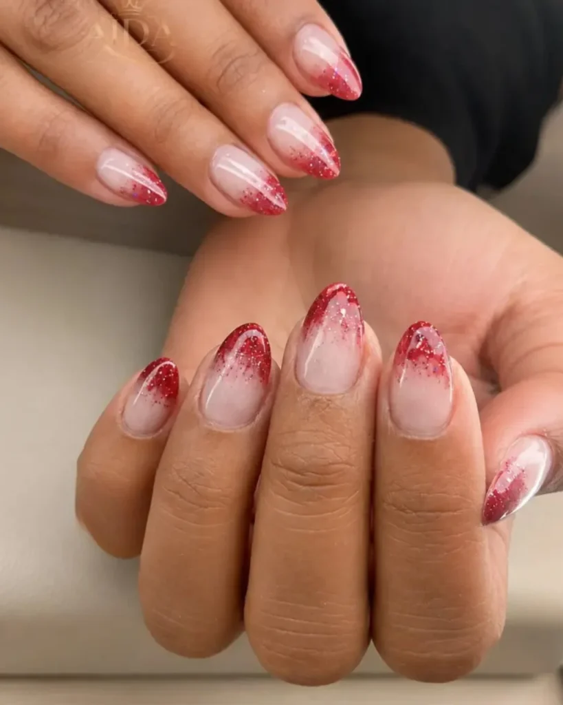Christmas glitter ombre nails with a sheer nude-pink base, red glitter fading across the tips, and elegant almond-shaped nails.