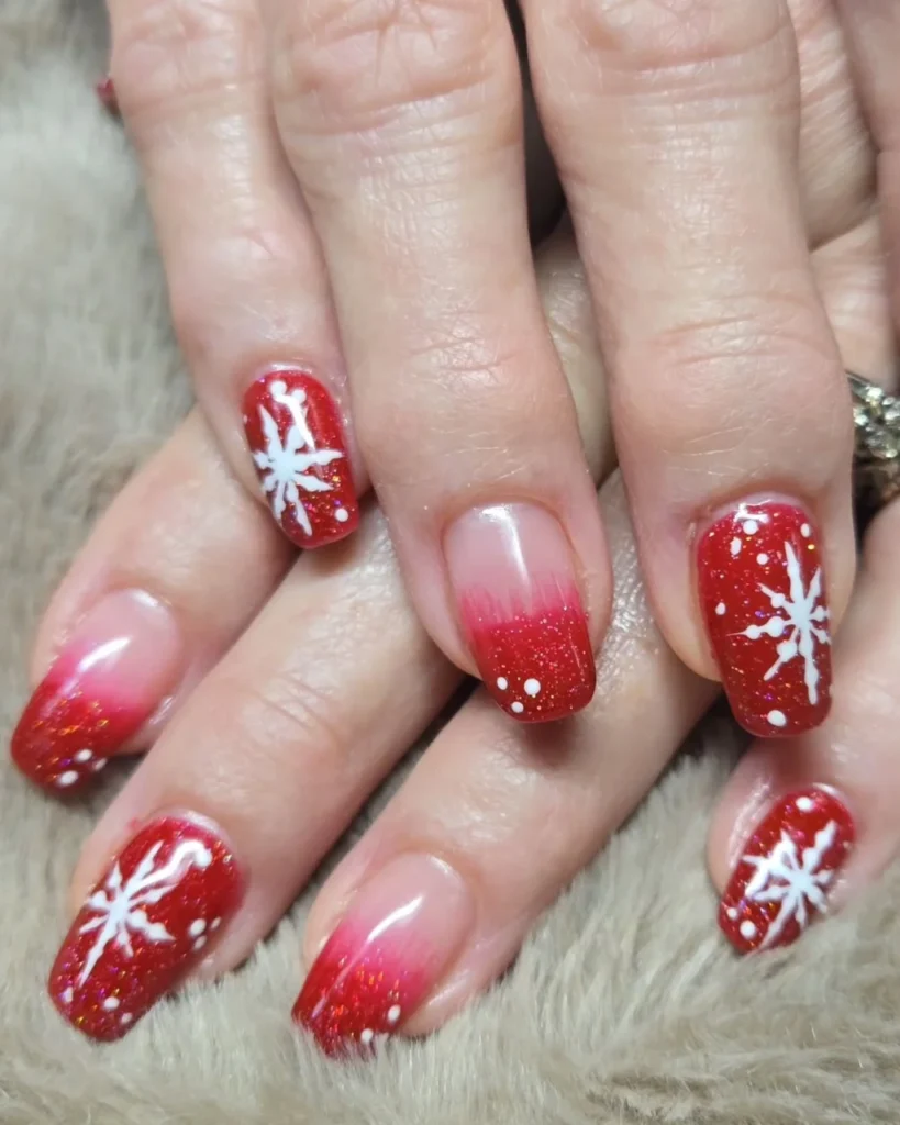 Christmas glitter ombre nails with red glitter tips, a sheer pink base, and hand-painted white snowflakes.