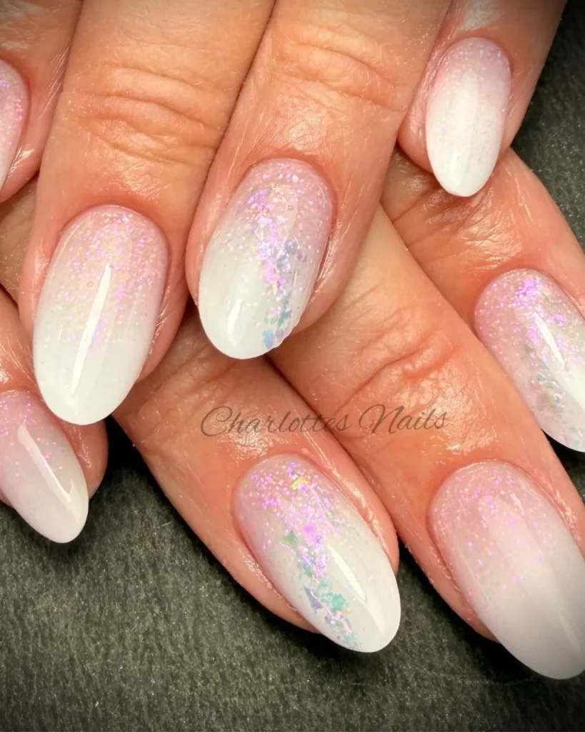 Christmas glitter ombre featuring a milky white base, soft pink shimmer, and iridescent glitter flakes on almond-shaped nails.