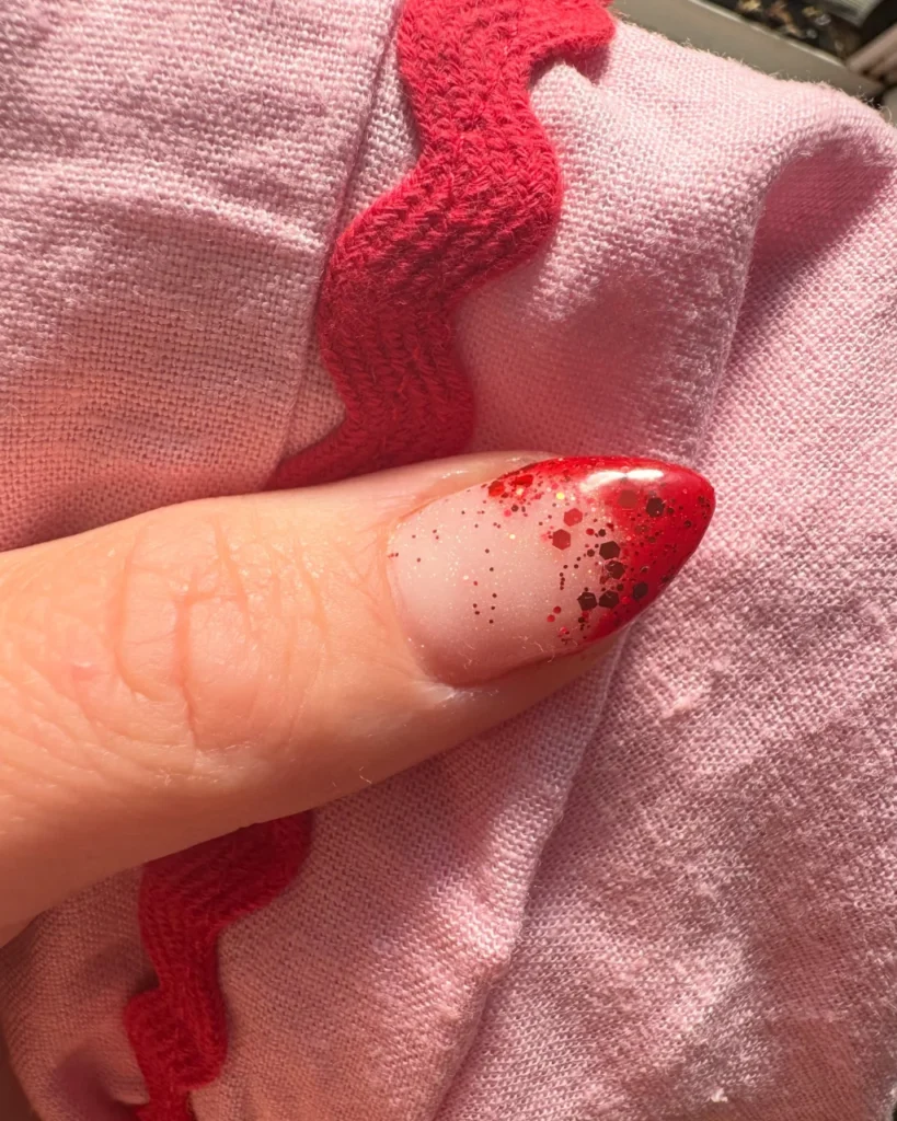 Christmas glitter ombre nail with red glitter fading from a nude base to sparkling red tips.
