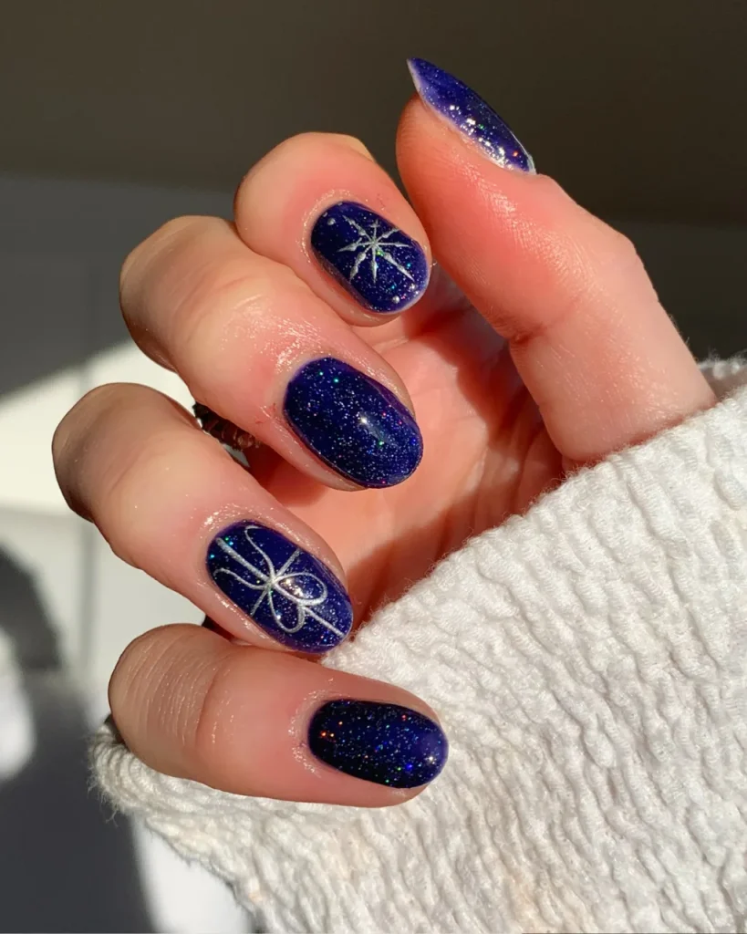 Classy Christmas short nail designs with deep navy blue glitter polish, delicate silver snowflakes, and fine gift-bow nail art.