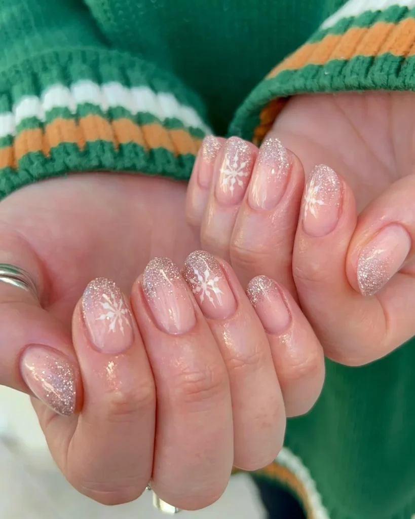 Classy Christmas short nail designs with sheer pink polish, delicate white snowflakes, and sparkling champagne glitter tips.