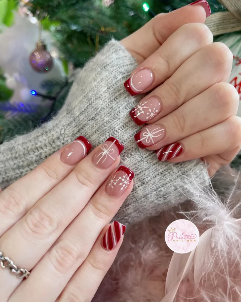 Classy Christmas short nail designs with glossy red French tips, nude pink bases, delicate white snowflakes, gift bows, and candy-cane stripes.