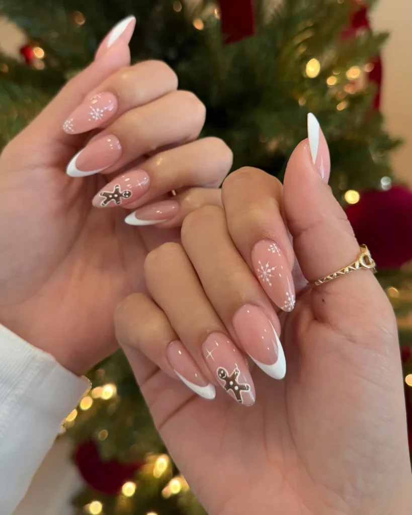 French manicure Christmas nail designs with pink almond nails, white French tips, delicate snowflakes, and brown gingerbread man nail art.