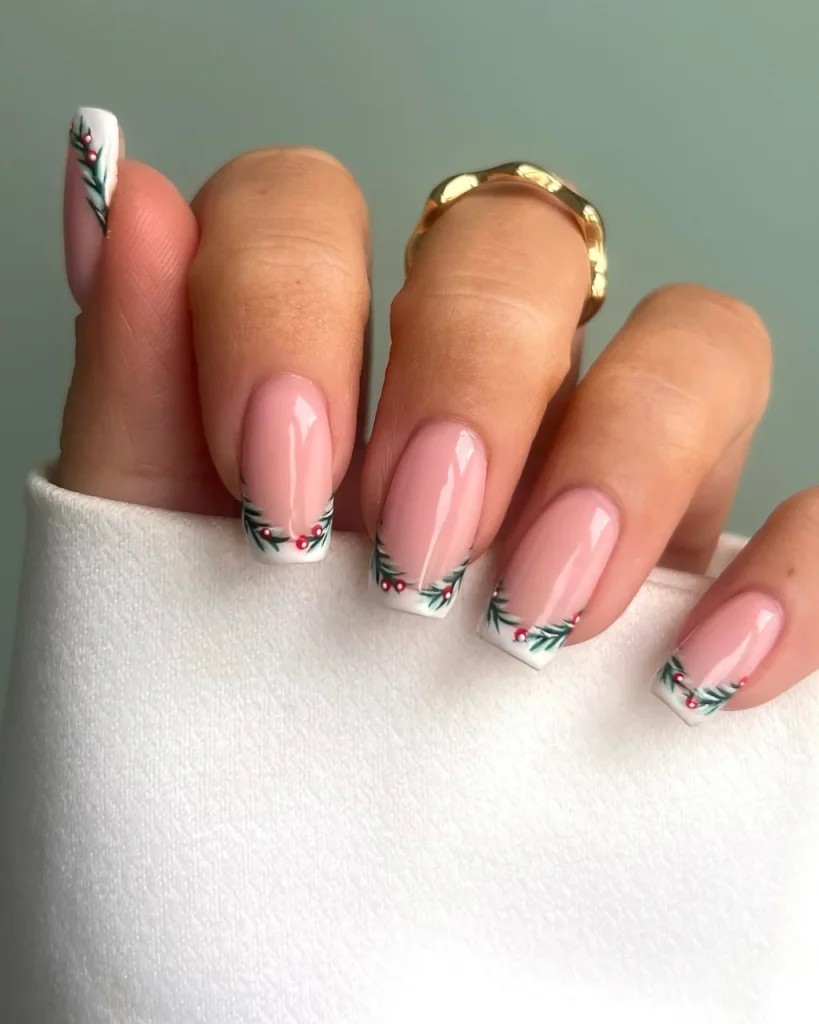 French manicure Christmas nail designs with sheer pink nails, white French tips, green holly leaves, and tiny red berries.