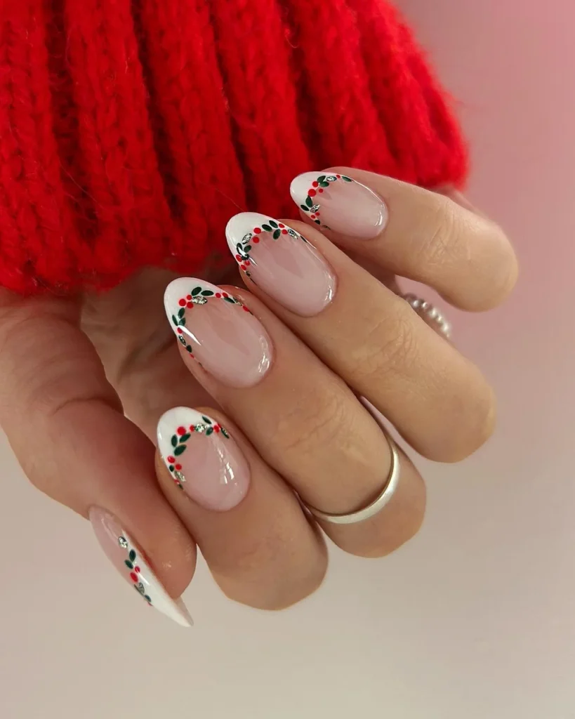 French manicure Christmas nail designs with nude pink almond nails, white French tips, green holly leaves, red berries, and delicate gold accents.