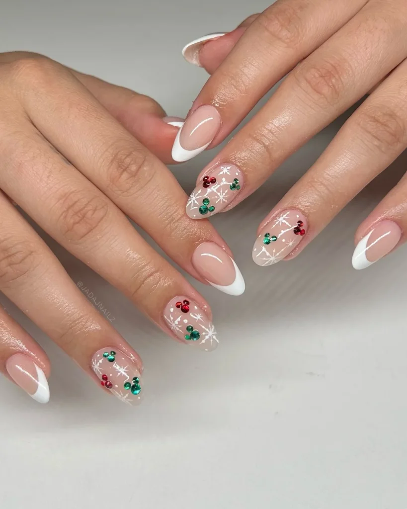 French manicure Christmas nail designs with glossy nude-pink nails, white French tips, delicate white snowflakes, and red and green rhinestone accents.