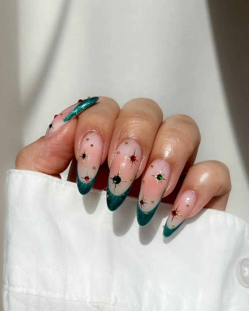 Green Christmas French tip nail designs with teal glitter tips, red and green starburst nail art, and tiny gold accents on a sheer pink base.
