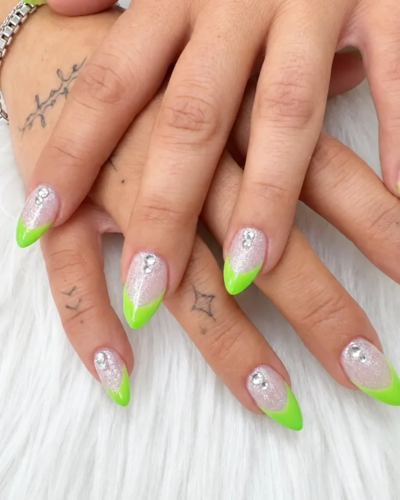 Green Christmas French tip nail designs with neon lime green tips, silver glitter bases, and sparkling rhinestone accents on almond-shaped nails.