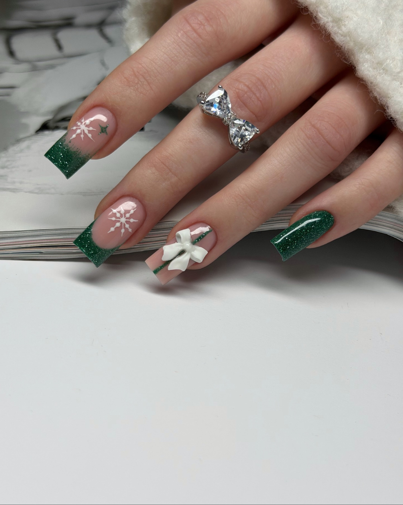 Green Christmas French tip nail designs with dark green glitter tips, white snowflakes, a 3D white bow, and a glossy nude pink base.