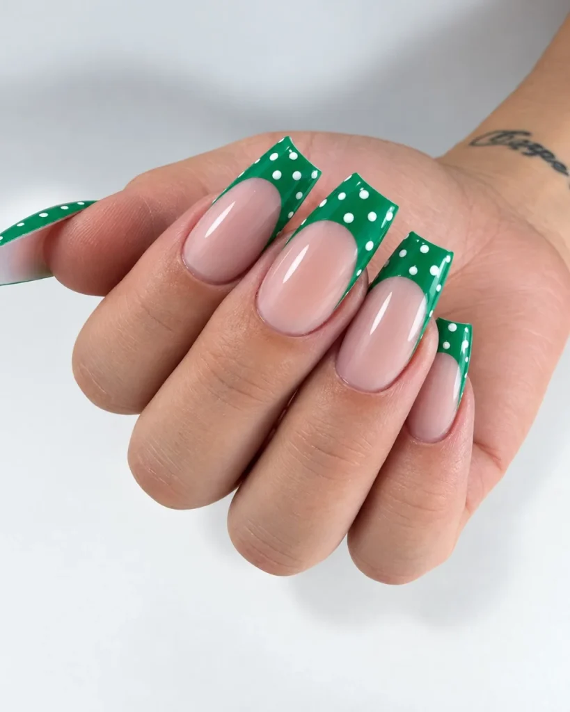 Green Christmas French tip nail designs with emerald green square tips, white polka dots, and a glossy nude pink base.