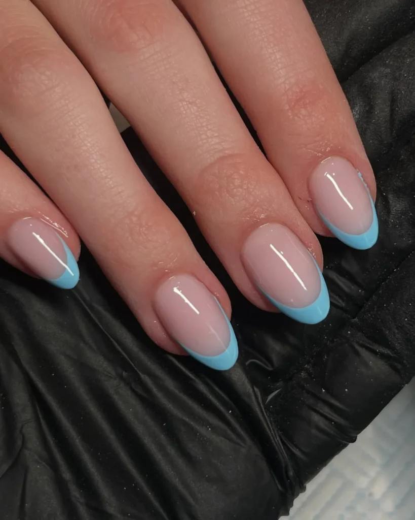Light blue nail designs with glossy nude pink bases and bright blue French tips on almond-shaped nails.