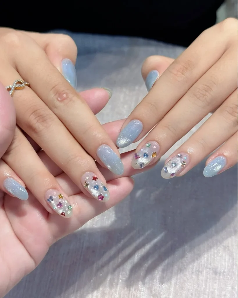 Light blue Christmas nail designs with icy blue glitter polish and nude accent nails decorated with colorful stars and festive glitter.