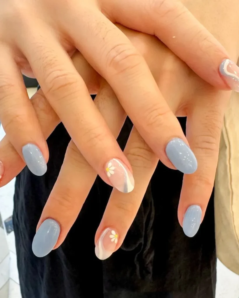 Light blue nail designs with glossy pastel blue polish, nude accent nails, delicate white daisies, and curved French tip details.