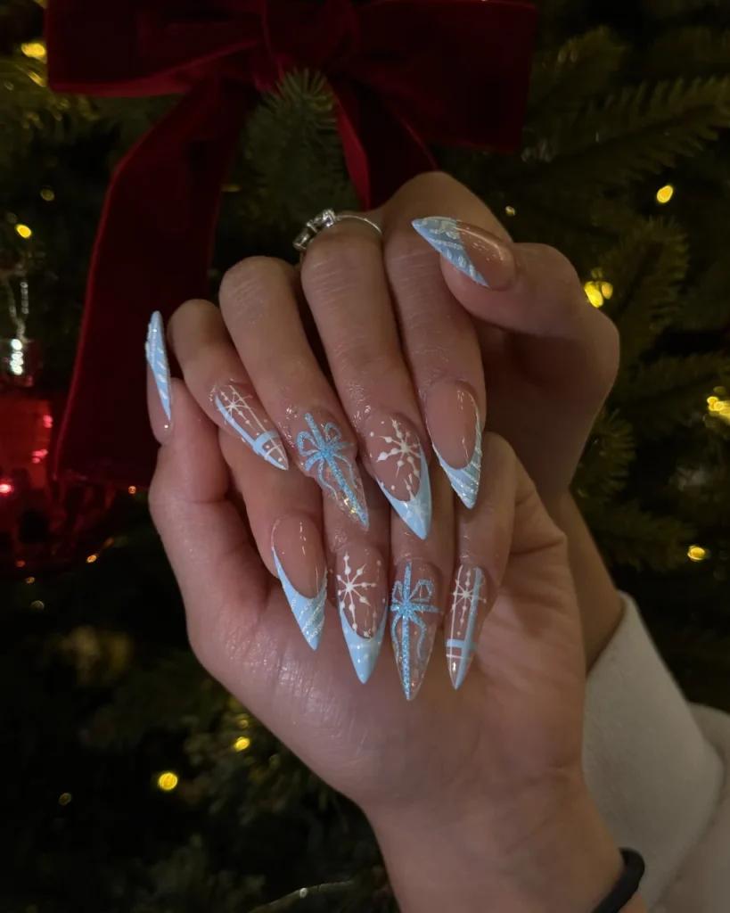 Light blue Christmas nail designs with white snowflakes, glittery blue gift bows, present patterns, and diagonal French tips on long stiletto nails.