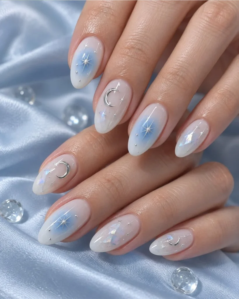 Light blue Christmas nail designs with icy blue ombre, silver crescent moons, delicate stars, and subtle rhinestone accents on almond-shaped nails.