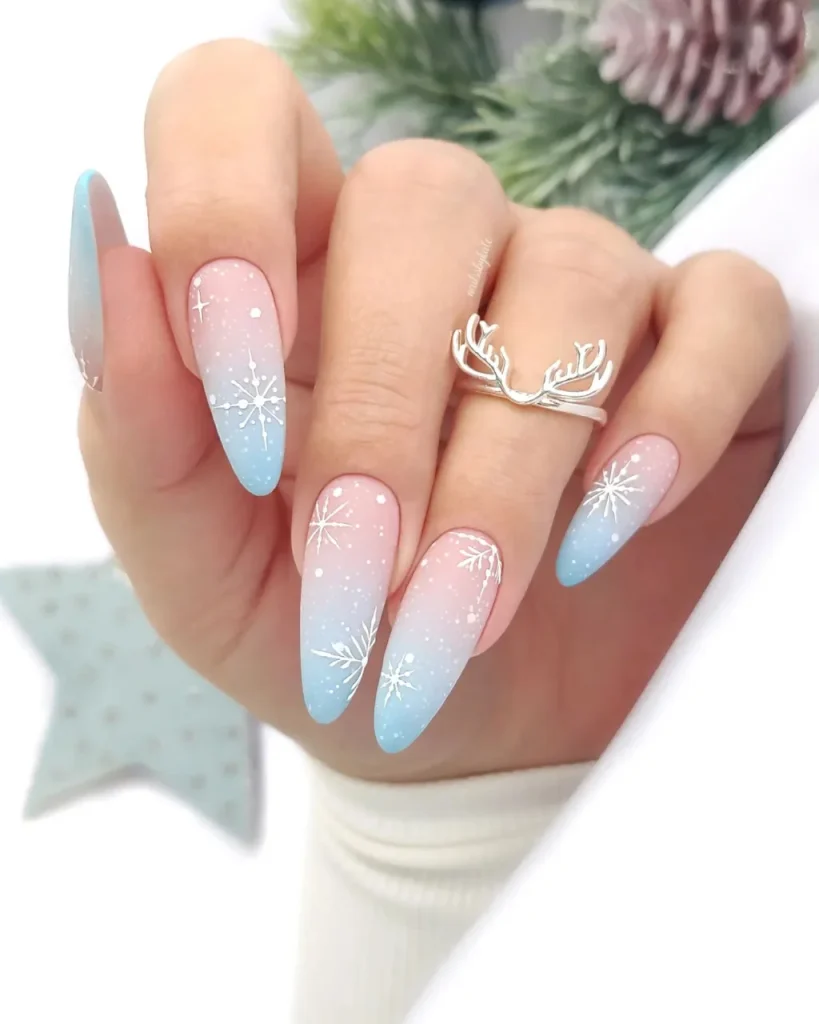 Light blue Christmas nail designs with pink-to-blue ombre, white snowflakes, delicate star details, and long almond-shaped nails.