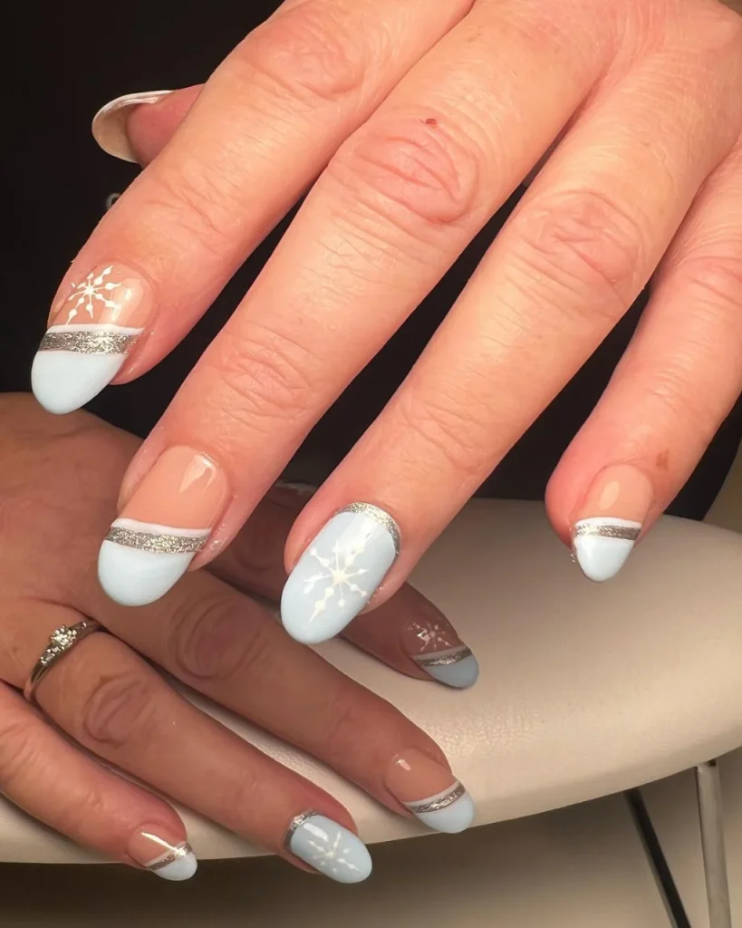 Light blue Christmas nail designs with white snowflakes, gold glitter stripes, and nude French tips.