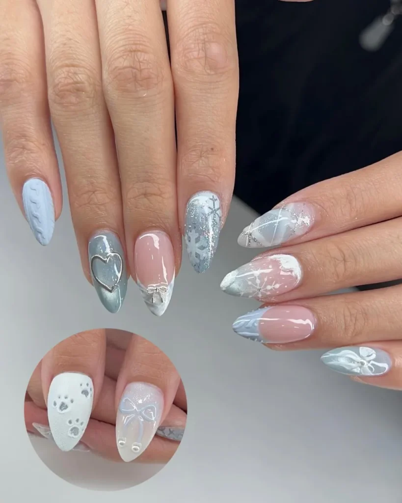 Light blue Christmas nail designs featuring white snowflakes, knitted nail art, silver glitter, heart accents, and pink ombre details on almond-shaped nails.