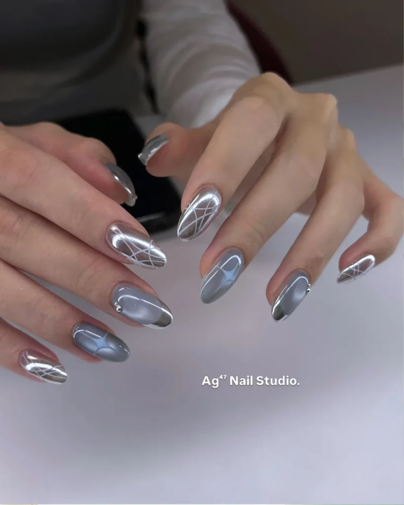 Light blue and silver chrome Christmas nail designs with geometric white lines and glossy metallic accents on almond-shaped nails.