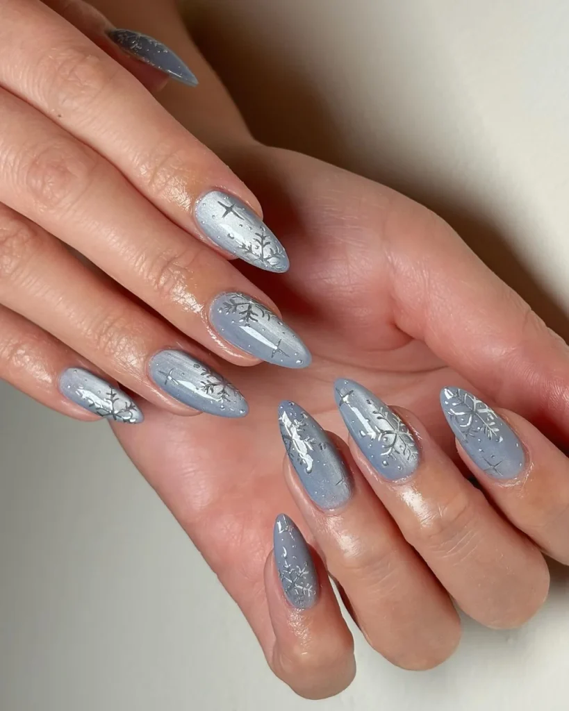Light blue Christmas nail designs with intricate silver snowflakes, frosty branch details, and shimmering accents on long almond-shaped nails.