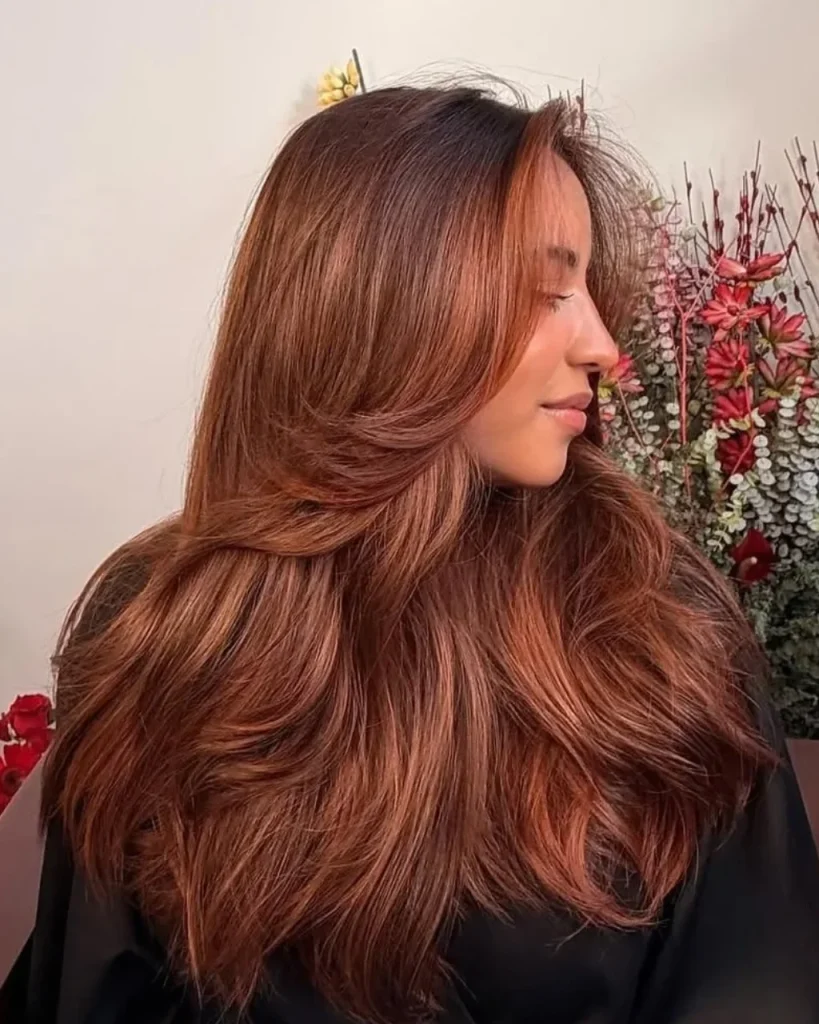 Light brown cinnamon hair color with warm copper balayage and face-framing highlights on long layered waves