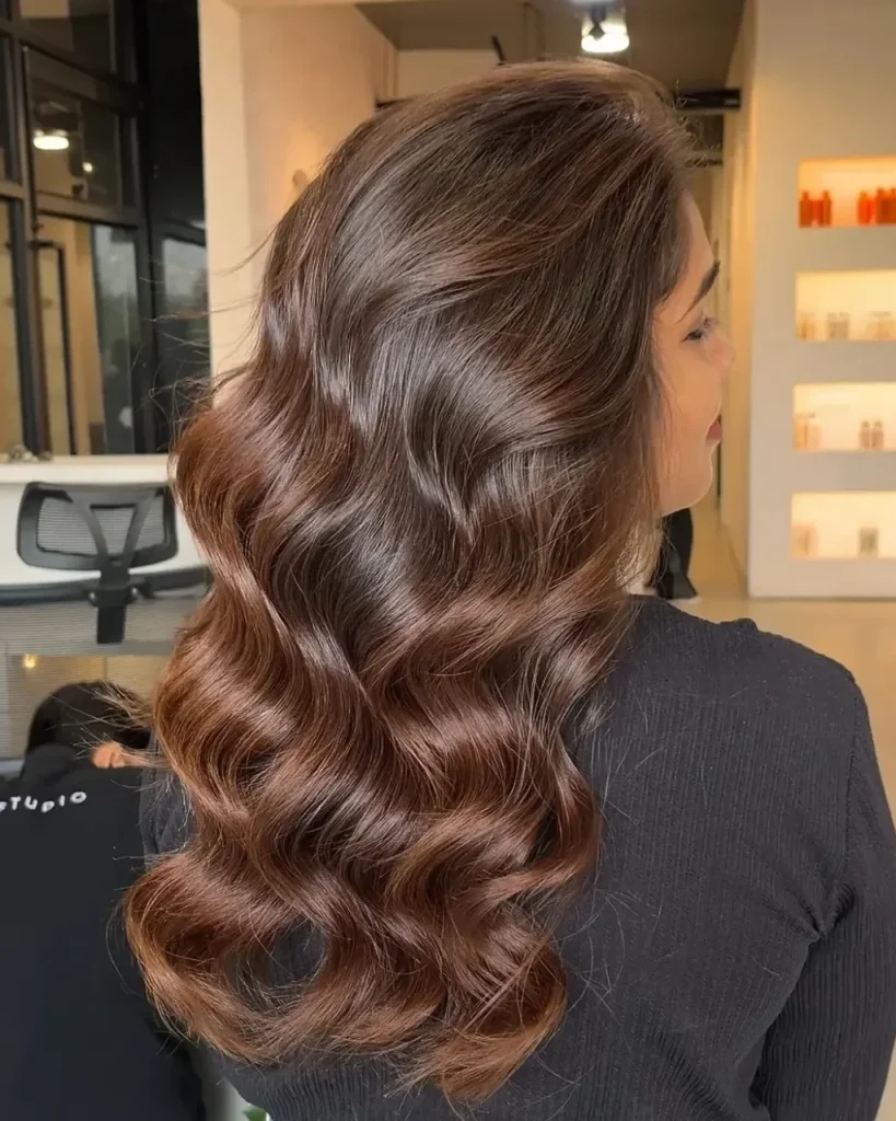 Light brown cinnamon hair color with soft copper balayage and glossy, voluminous curls