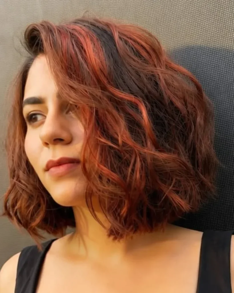 Light brown cinnamon hair with vibrant copper-red highlights on a textured bob for deeper skin tones