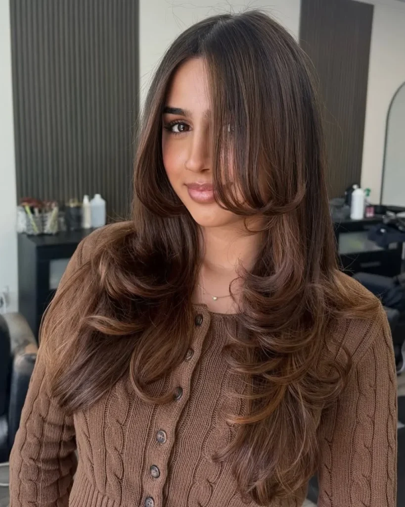 Light brown cinnamon hair with subtle warm highlights, long layers, and curtain bangs