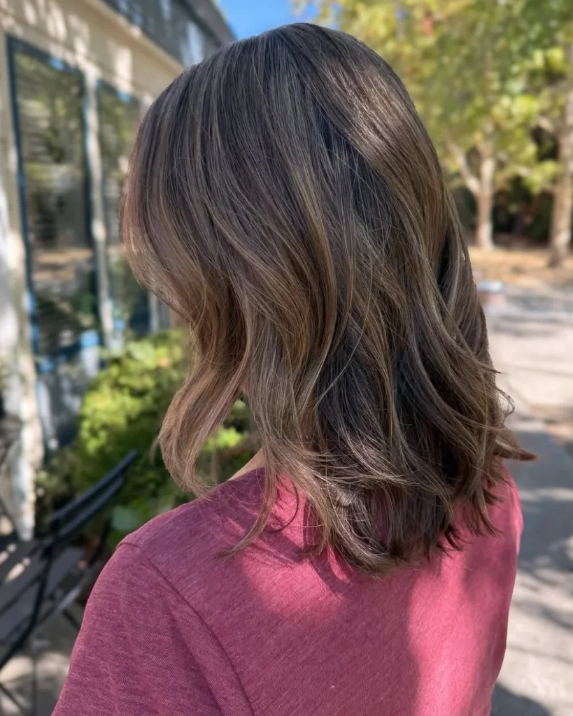 Light chocolate bronde hair with soft beige-brown highlights, dark roots, and loose layered waves