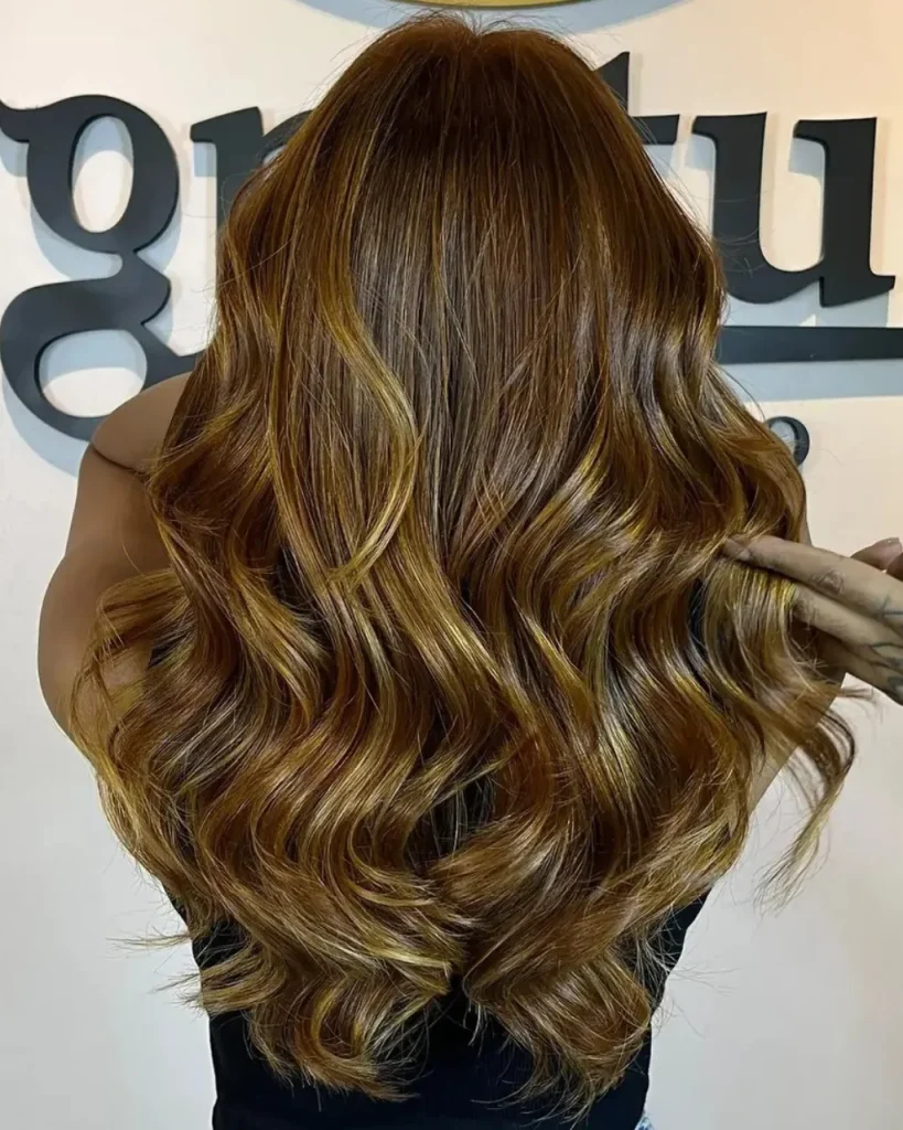 Light golden brown balayage with caramel and honey-gold highlights on long, glossy wavy hair.