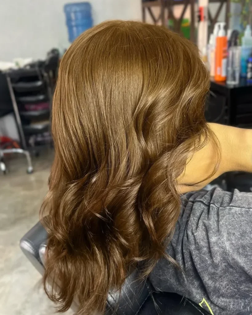 Light golden brown hair color with honey-gold highlights and glossy, voluminous waves