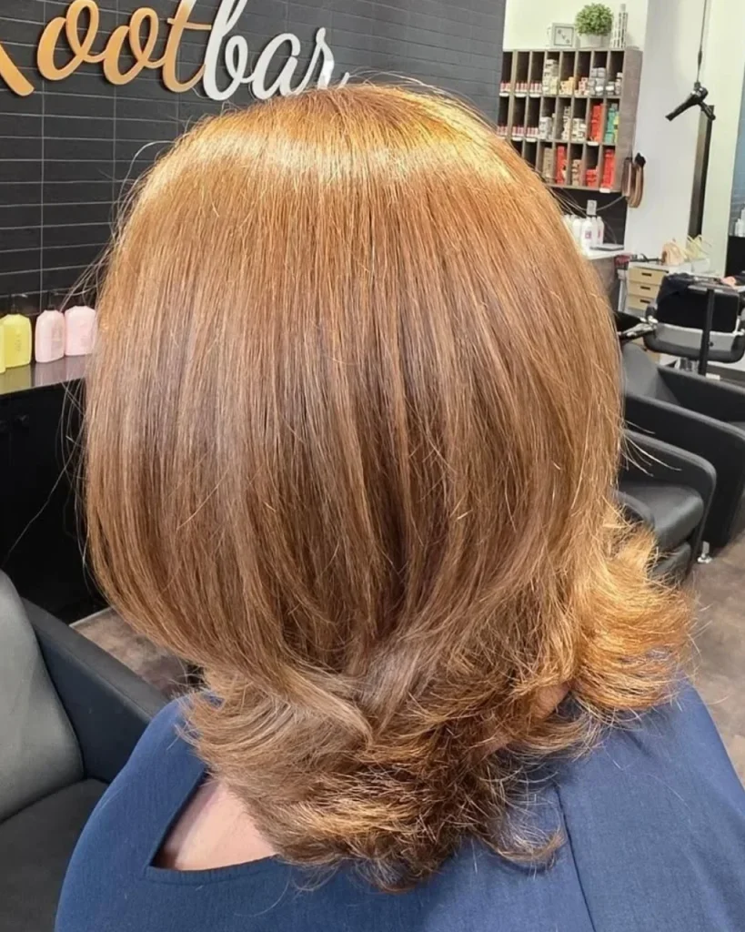 Light golden brown hair color with honey-caramel tones, feathered layers, and a voluminous shoulder-length blowout.