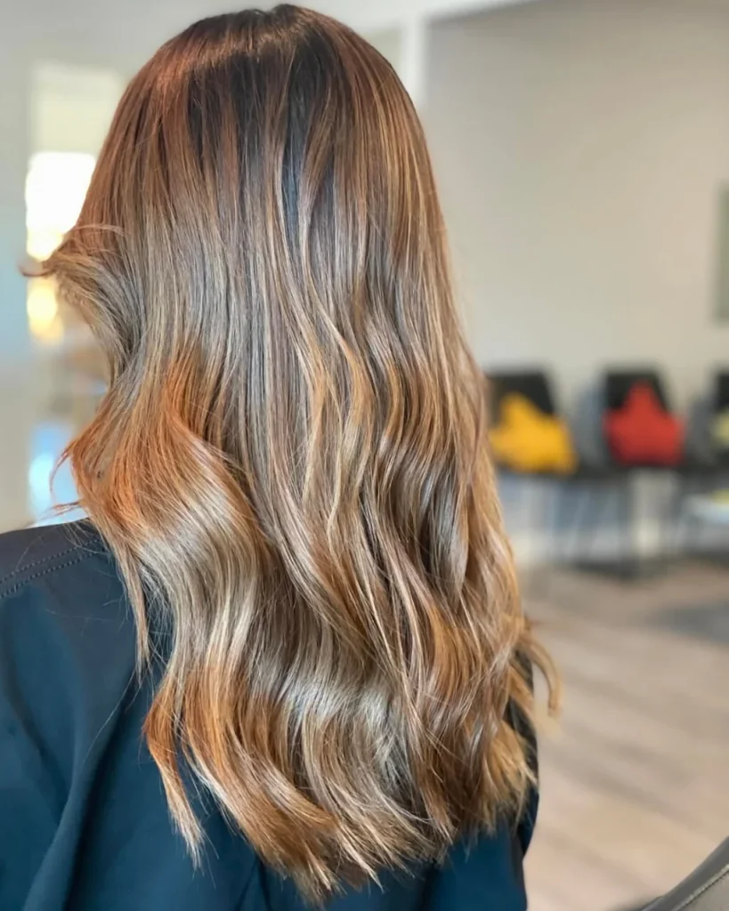 Light golden brown hair color with golden blonde money-piece highlights, caramel ribbons, and long glossy waves.