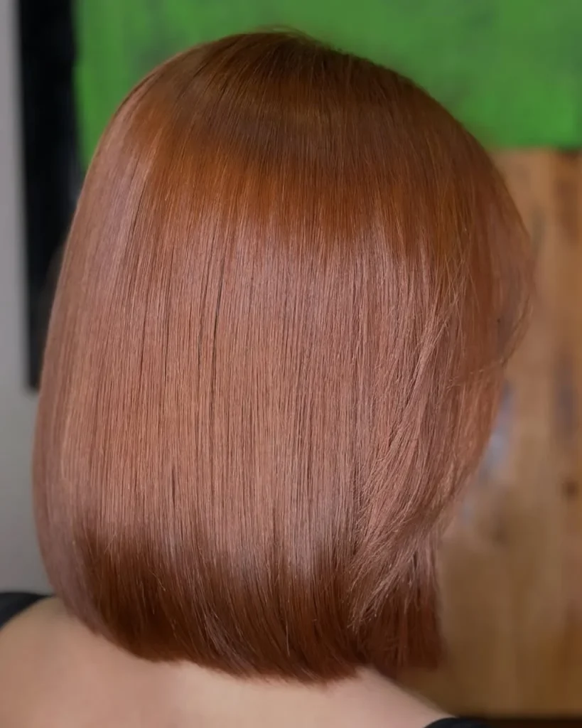 Light golden brown hair color with warm copper-golden tones on a sleek, chin-length lob haircut.