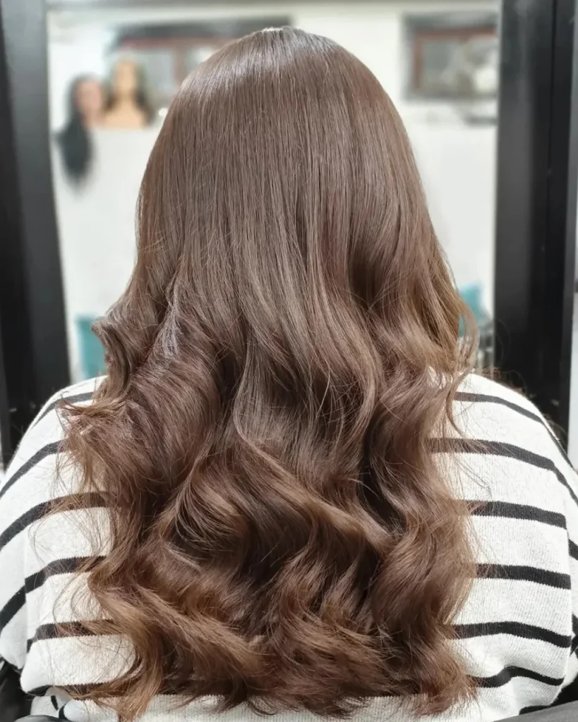 Light golden brown hair color with subtle golden highlights styled in long, voluminous waves.