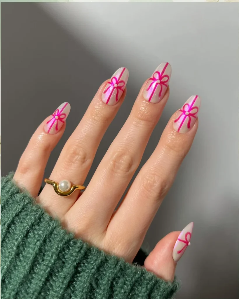 Light pink Christmas nails with delicate coquette bows on a sheer blush-pink base and a glossy festive finish.