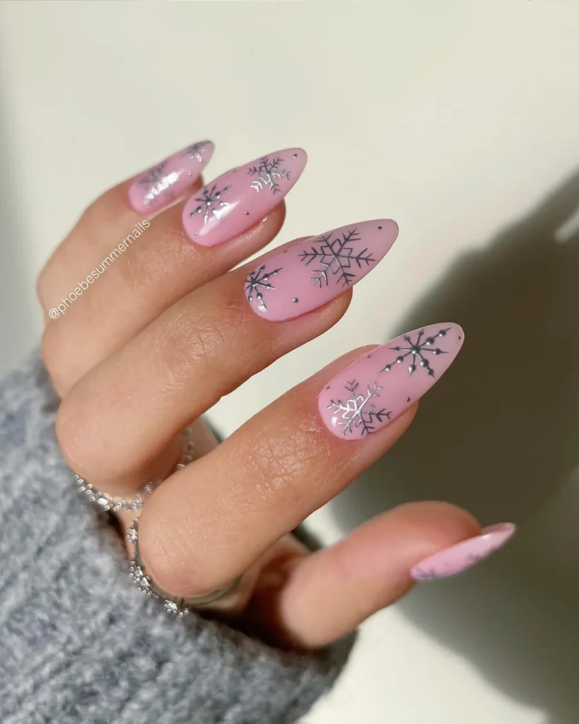 Light pink Christmas nails with delicate silver snowflakes and reflective chrome accents for a frosty festive manicure.