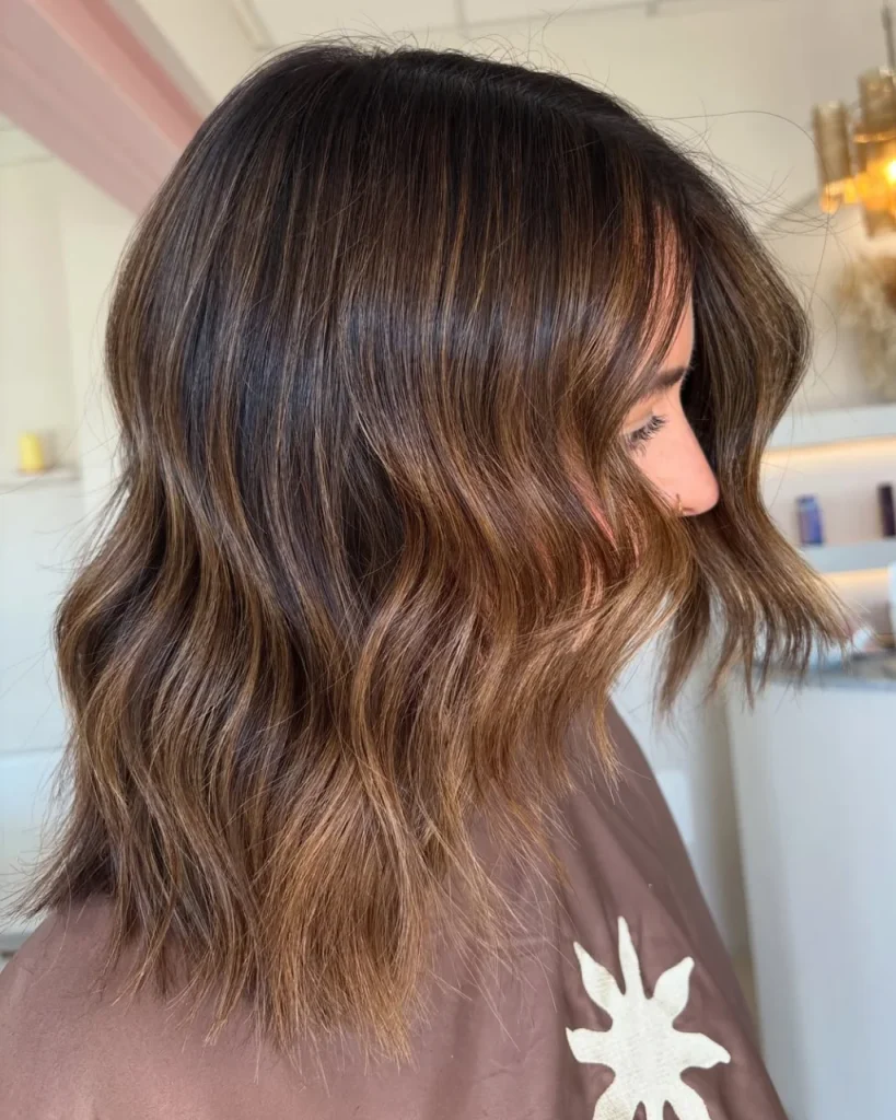 Medium length light brown hair color with caramel balayage, soft waves, and layered ends.