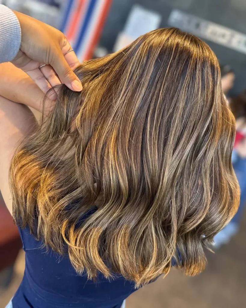Medium length light brown hair with golden highlights and soft shoulder-length waves.