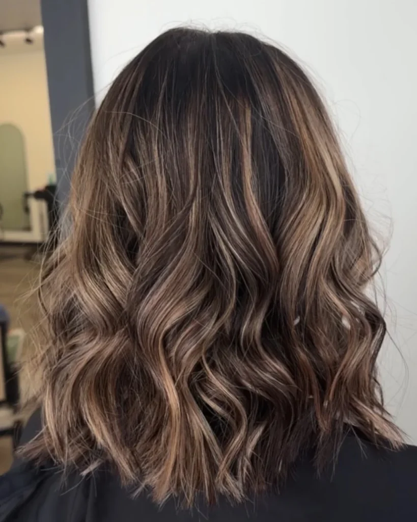 Medium length light brown hair in a cool mushroom brown shade with smoky highlights and soft waves.