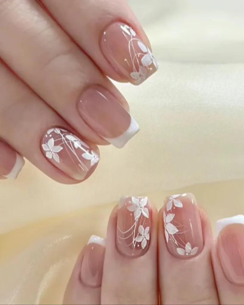 Short french tip christmas nail designs with a sheer nude pink base, white French tips, and delicate white floral nail art.