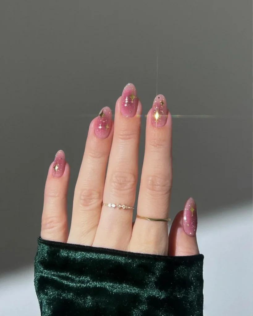 Pink aura Christmas nails with a soft diffused pink gradient and delicate golden star accents for a luminous festive manicure.