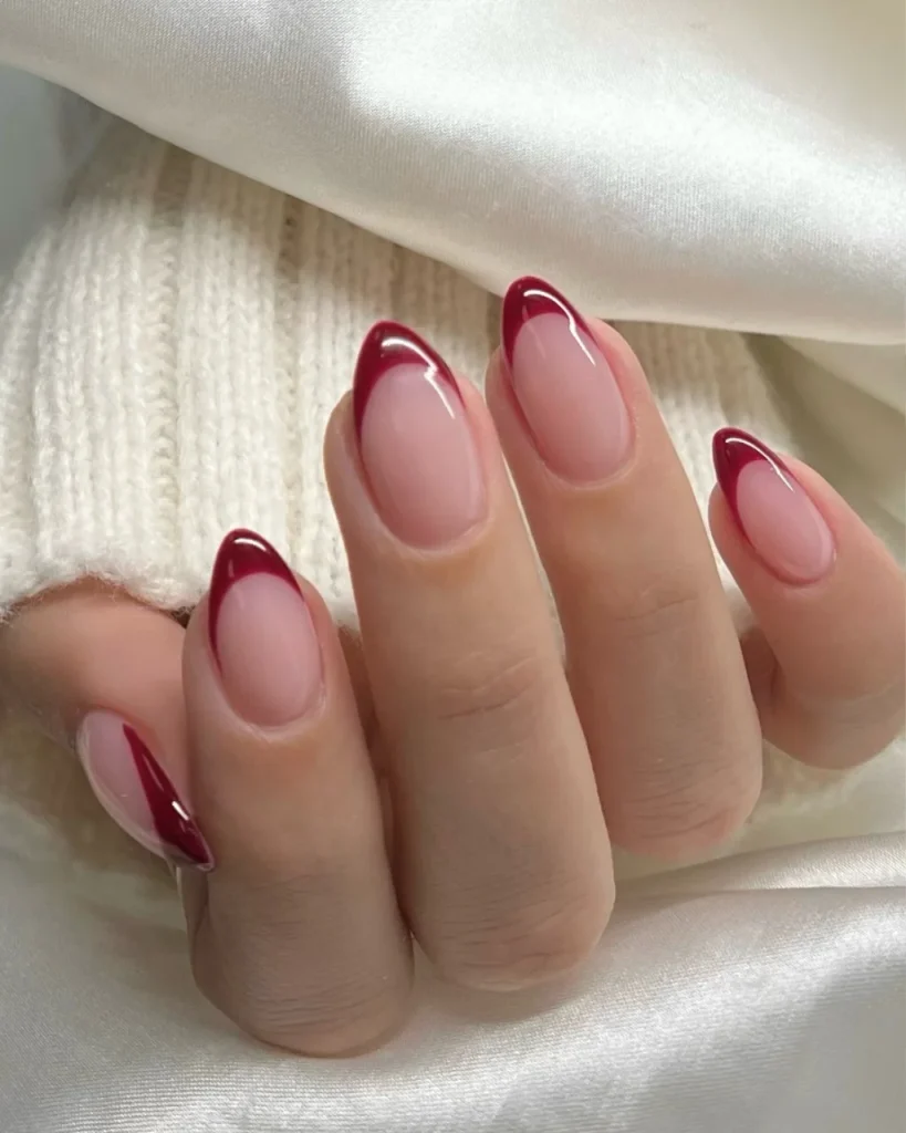 Red French tip Christmas nail designs featuring glossy burgundy tips on a sheer pink base with elegant almond-shaped nails for a chic festive manicure.