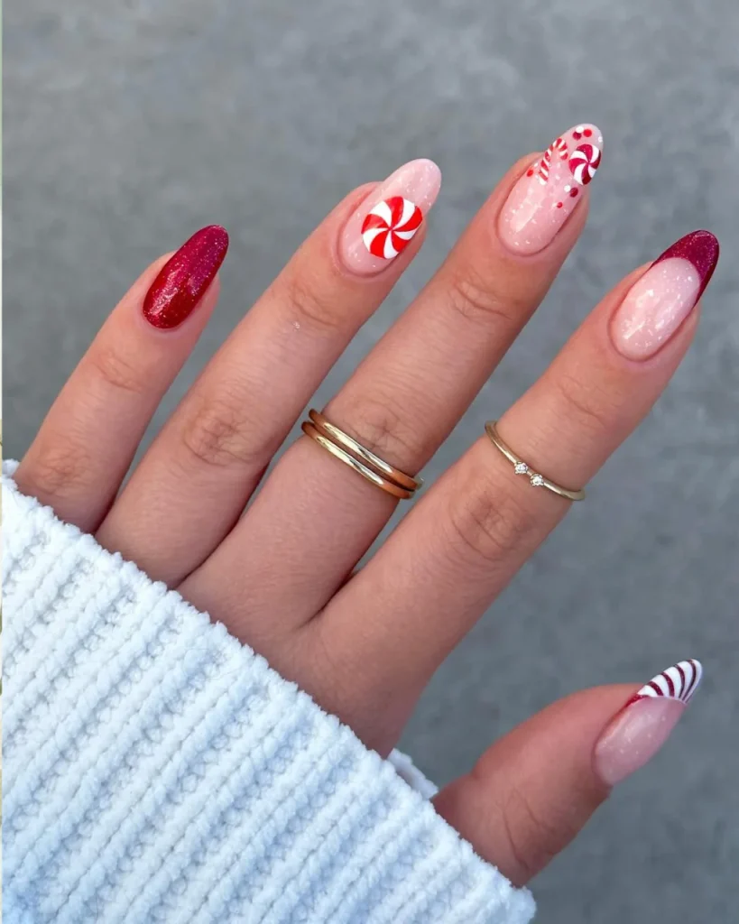 Red French tip Christmas nail designs with candy cane stripes, peppermint swirl nail art, and sparkling red glitter on pink almond-shaped nails.
