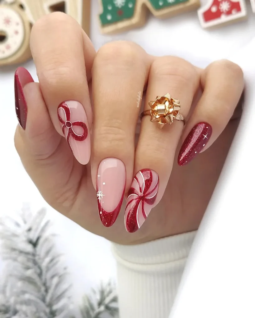 Red French tip Christmas nail designs featuring burgundy glitter tips, glossy pink almond-shaped nails, a red gift bow, peppermint swirl nail art, and delicate white snowflake accents.