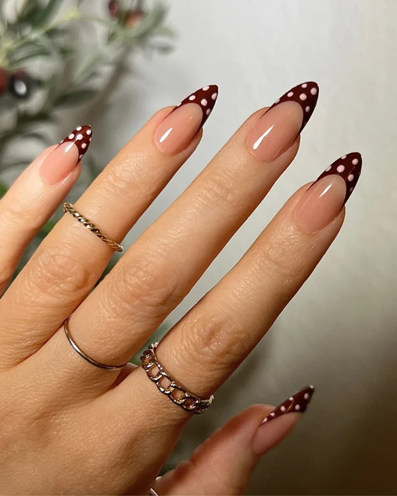 Red French tip Christmas nail designs with burgundy polka-dot tips on nude almond-shaped nails.
