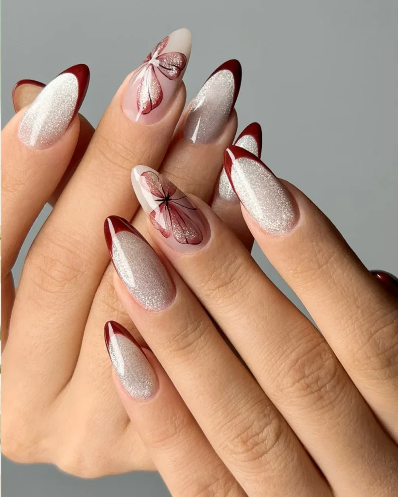 Red French tip Christmas nail designs with silver glitter, deep red tips, and delicate butterfly nail art on almond-shaped nails.